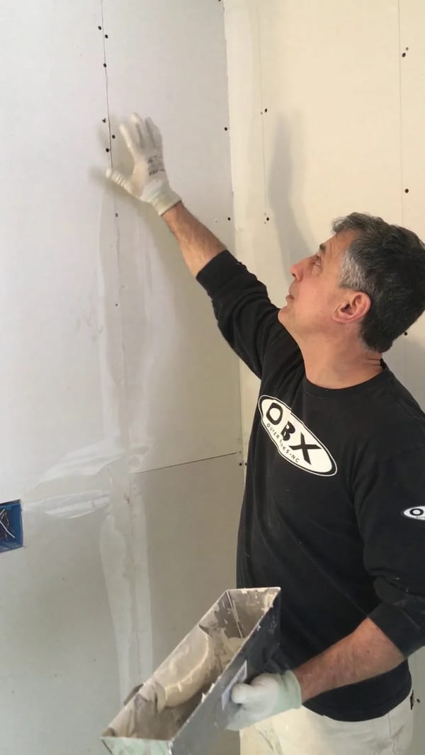 Drywall installer lifting a sheet of drywall onto a wall